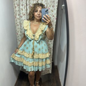Vestido boho corto turquesa con bordados dorados, escote en pico con volantes beige y estilo romántico de verano.