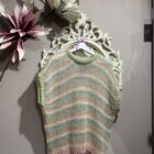 Chaleco de punto de rayas multicolor en tonos pastel rosa, verde y azul combinado con camisa blanca y vaqueros.